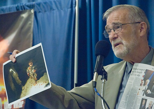 Ex-CIA analyst Ray McGovern holding up the iconic photograph of a six-year-old Iraqi girl who survived the accidental killing of her parents by U.S. troops in 2004. (Photo credit: Stars and Stripes.)