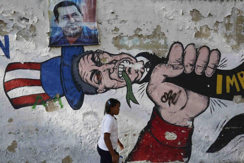 A Venzuelan woman walks by anti-American graffiti and a portrait of Hugo Chavez in Caracas.